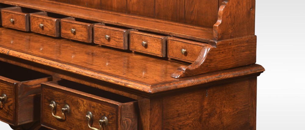 A warm brown Georgian style oak dresser featuring an upper open plate rack with a shaped frieze above three base drawers and cabriole legs. View V