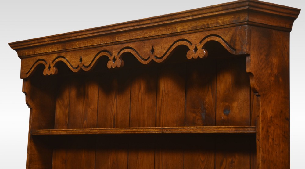 A warm brown Georgian style oak dresser featuring an upper open plate rack with a shaped frieze above three base drawers and cabriole legs. View VII