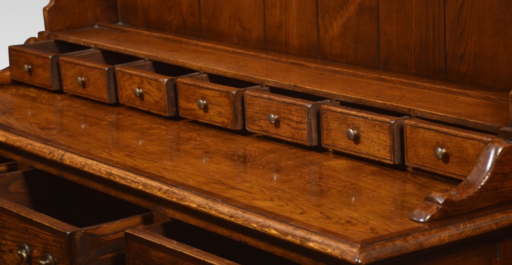 A warm brown Georgian style oak dresser featuring an upper open plate rack with a shaped frieze above three base drawers and cabriole legs. View IX