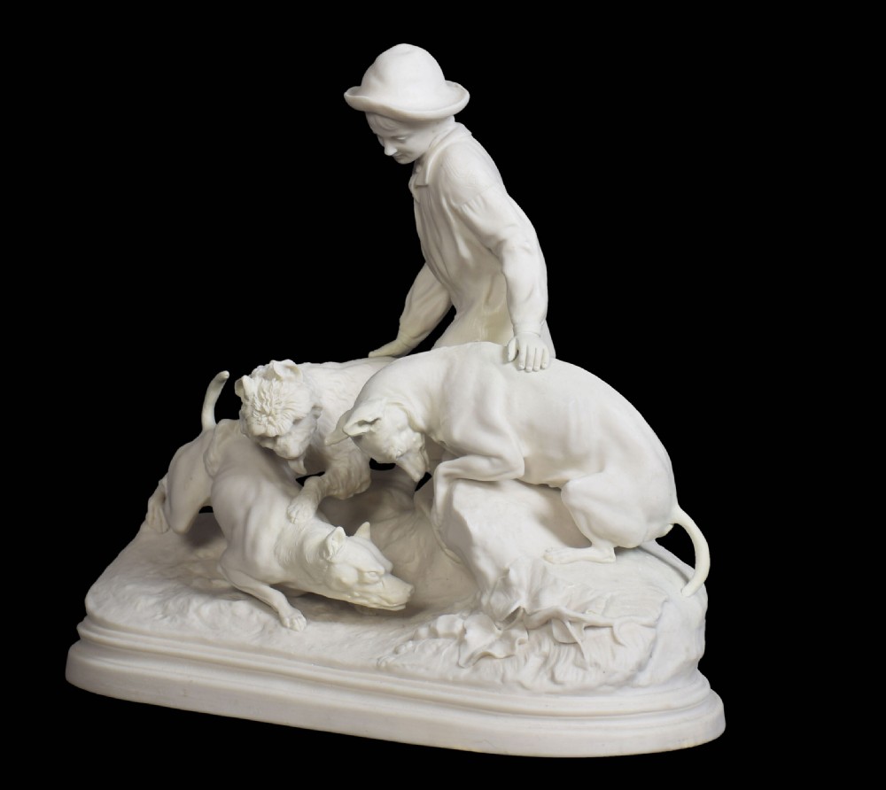 A white unglazed Victorian Parian ware sculpture depicting a young male figure leaning over three hounds on a moulded terrain base. View III
