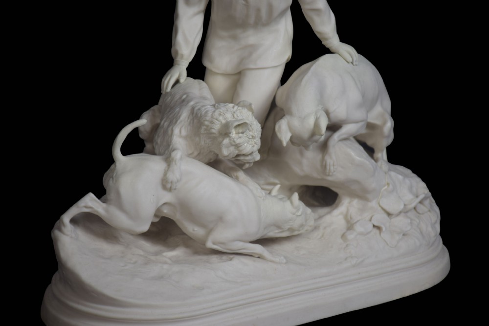 A white unglazed Victorian Parian ware sculpture depicting a young male figure leaning over three hounds on a moulded terrain base. View IV