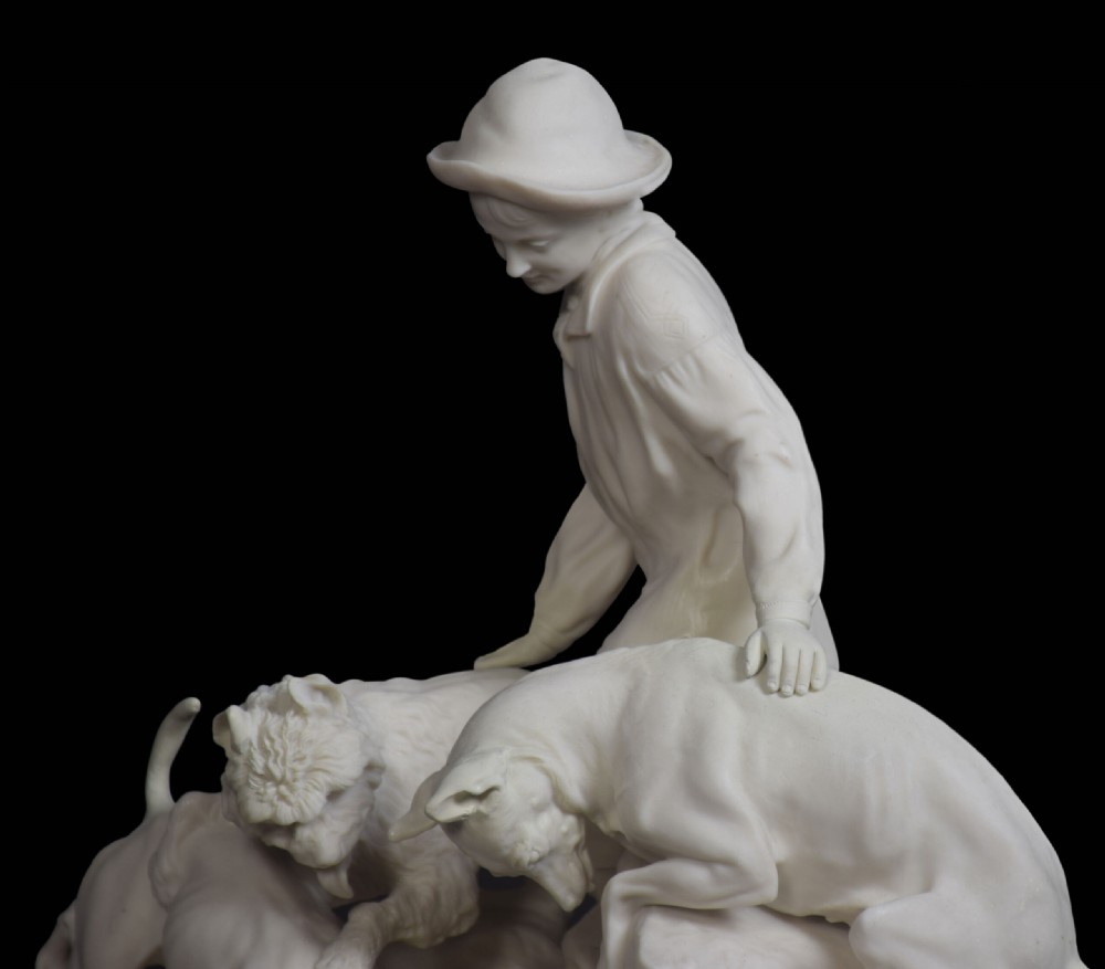 A white unglazed Victorian Parian ware sculpture depicting a young male figure leaning over three hounds on a moulded terrain base. View VI