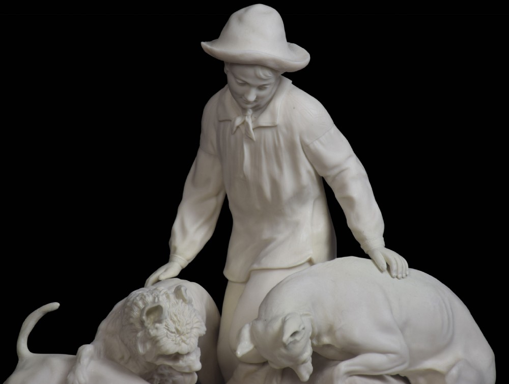 A white unglazed Victorian Parian ware sculpture depicting a young male figure leaning over three hounds on a moulded terrain base. View VII