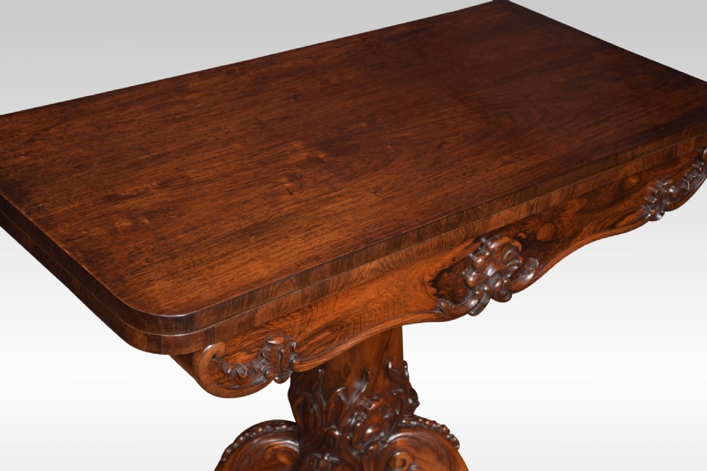 A Victorian dark rosewood fold-over card table featuring an ornate carved frieze, a central carved pedestal column, and carved scroll legs. View X