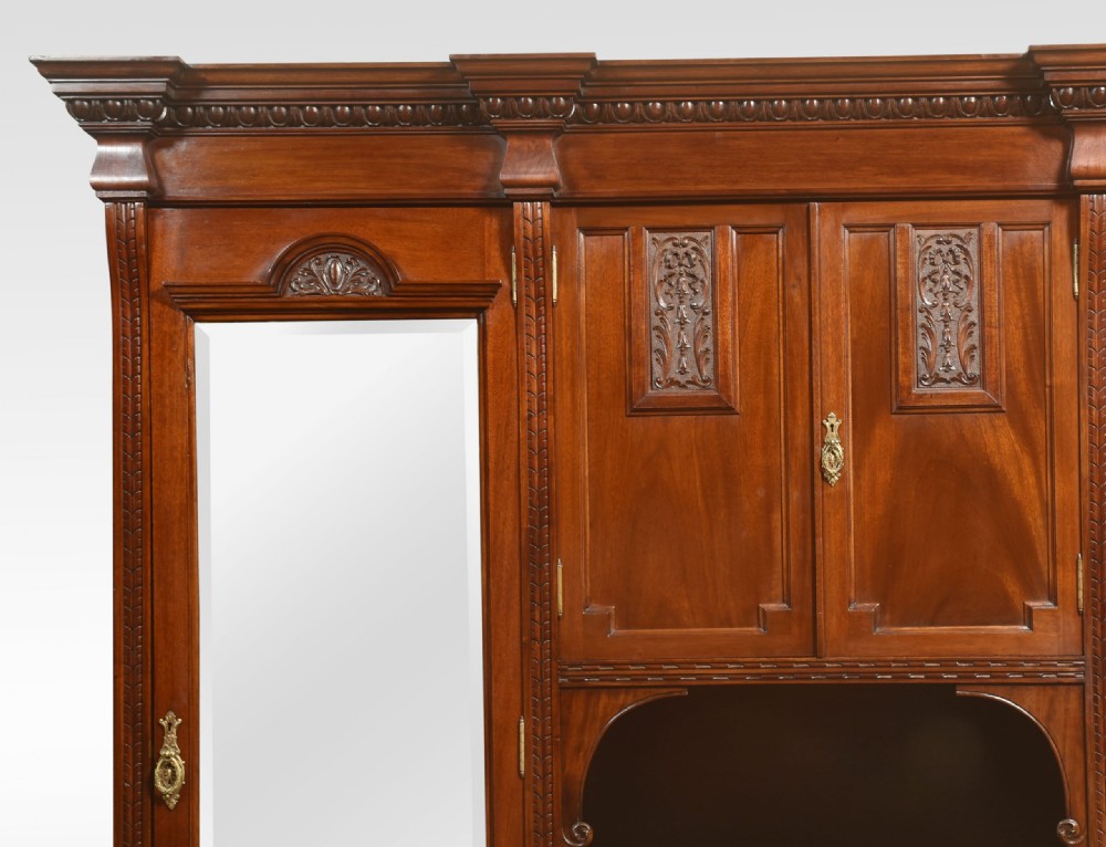 An antique carved mahogany compactum wardrobe featuring twin full-length mirrored doors flanking a central cupboard section, open niche, and multiple drawers with brass hardware. View II