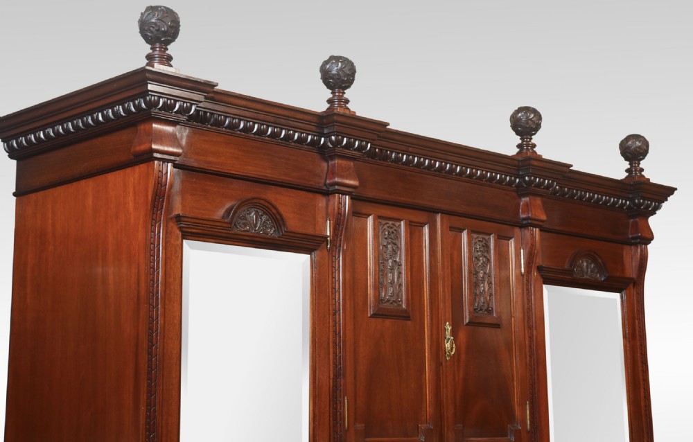 An antique carved mahogany compactum wardrobe featuring twin full-length mirrored doors flanking a central cupboard section, open niche, and multiple drawers with brass hardware. View X