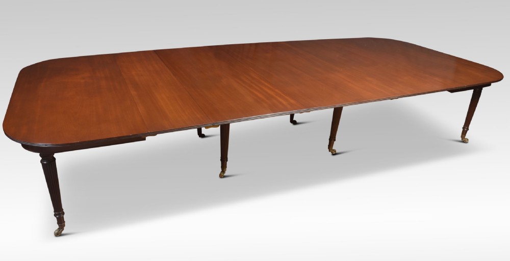 A large mahogany extending dining table featuring an imperial telescopic action, rounded corners, and reeded turned legs on brass castors.