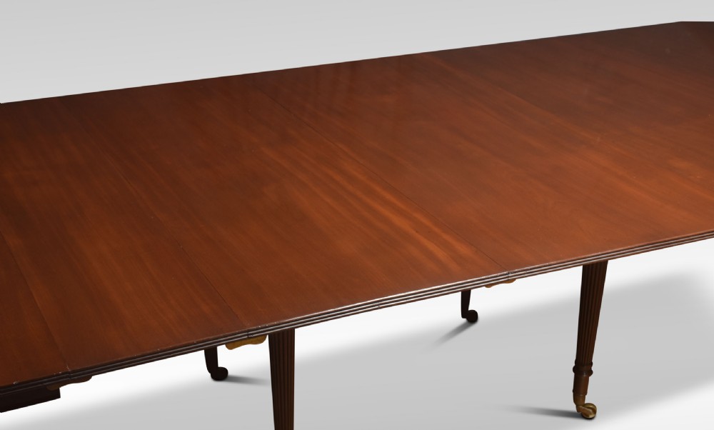 A large mahogany extending dining table featuring an imperial telescopic action, rounded corners, and reeded turned legs on brass castors. View II