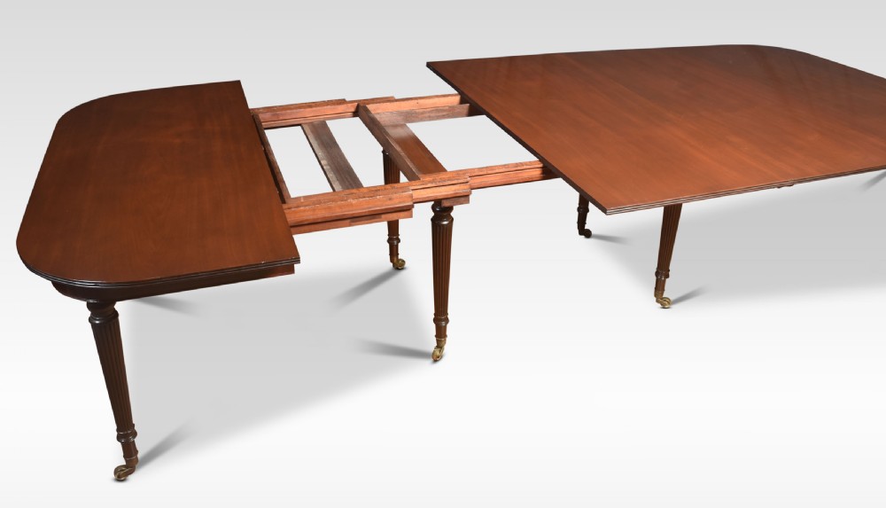 A large mahogany extending dining table featuring an imperial telescopic action, rounded corners, and reeded turned legs on brass castors. View V