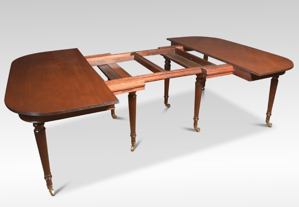 A large mahogany extending dining table featuring an imperial telescopic action, rounded corners, and reeded turned legs on brass castors. View VII