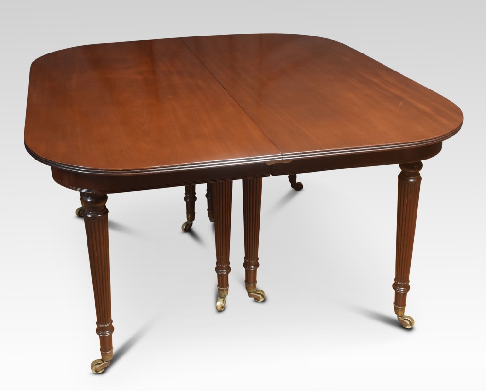 A large mahogany extending dining table featuring an imperial telescopic action, rounded corners, and reeded turned legs on brass castors. View VIII