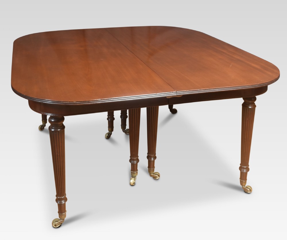A large mahogany extending dining table featuring an imperial telescopic action, rounded corners, and reeded turned legs on brass castors. View IX