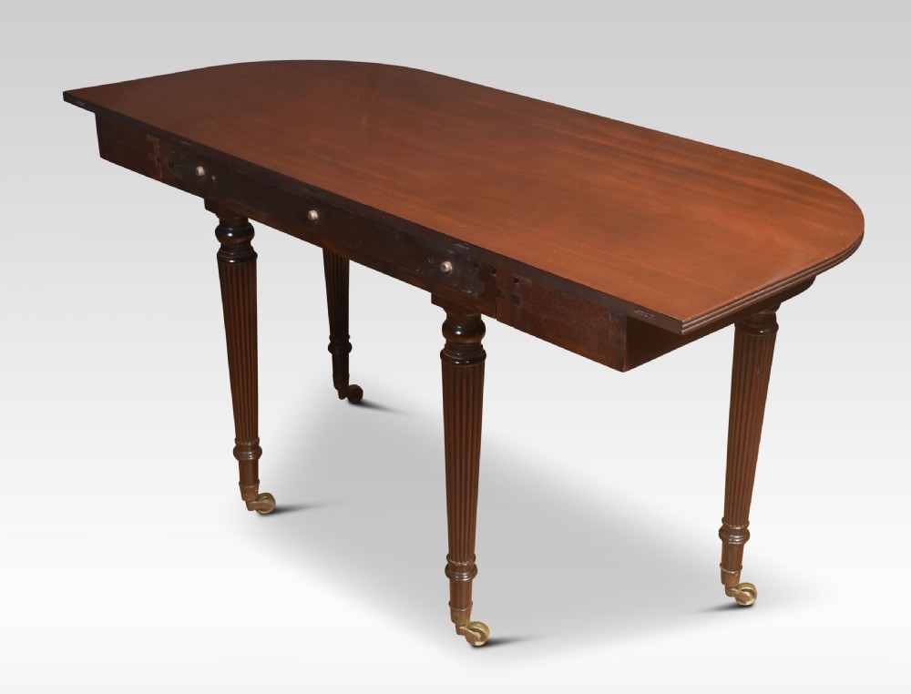 A large mahogany extending dining table featuring an imperial telescopic action, rounded corners, and reeded turned legs on brass castors. View X