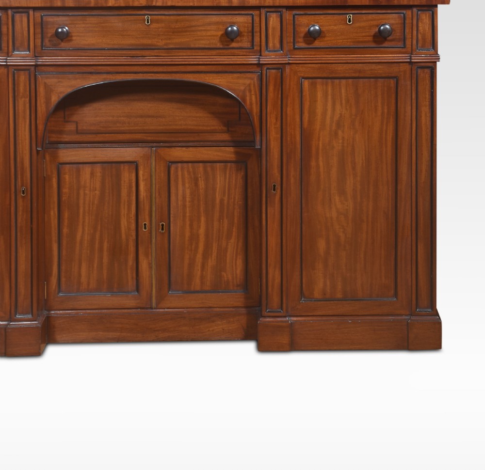 A Regency period warm brown mahogany sideboard featuring four cupboard doors, three top drawers, turned wooden knobs, and an arched central alcove. View II
