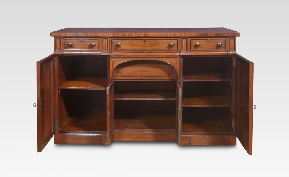 A Regency period warm brown mahogany sideboard featuring four cupboard doors, three top drawers, turned wooden knobs, and an arched central alcove. View III