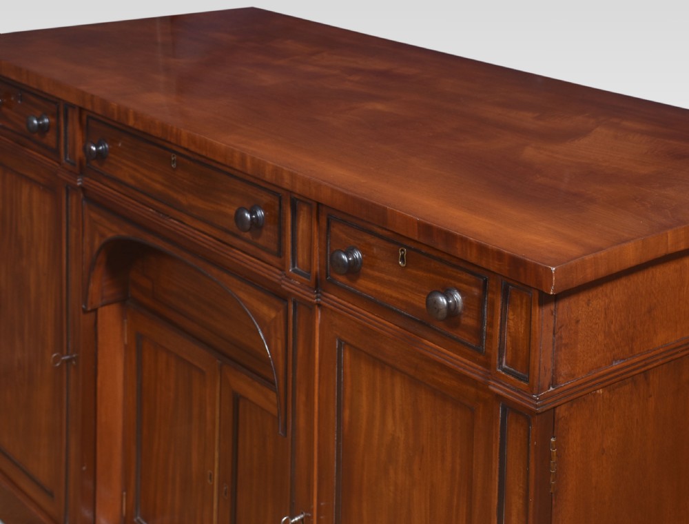 A Regency period warm brown mahogany sideboard featuring four cupboard doors, three top drawers, turned wooden knobs, and an arched central alcove. View V
