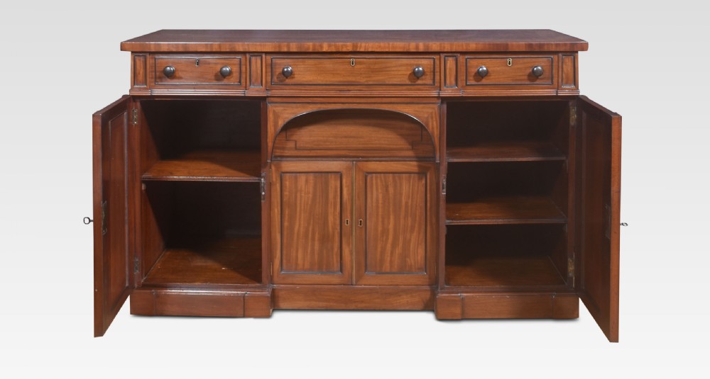 A Regency period warm brown mahogany sideboard featuring four cupboard doors, three top drawers, turned wooden knobs, and an arched central alcove. View VIII