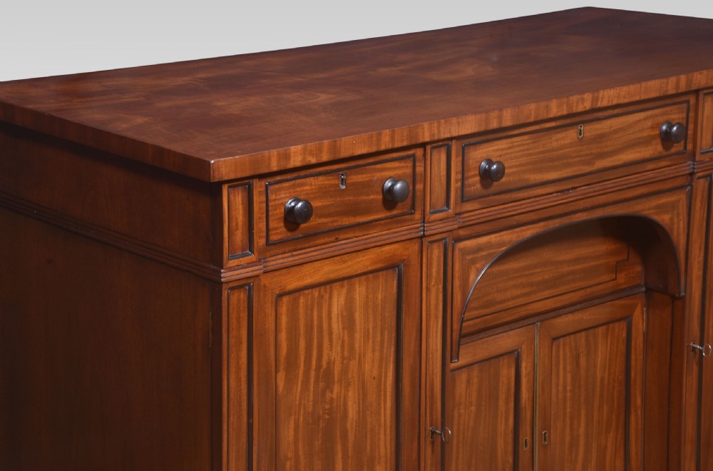 A Regency period warm brown mahogany sideboard featuring four cupboard doors, three top drawers, turned wooden knobs, and an arched central alcove. View IX