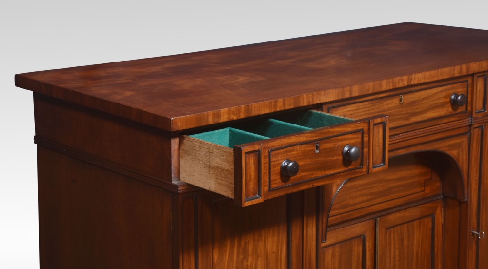 A Regency period warm brown mahogany sideboard featuring four cupboard doors, three top drawers, turned wooden knobs, and an arched central alcove. View XI