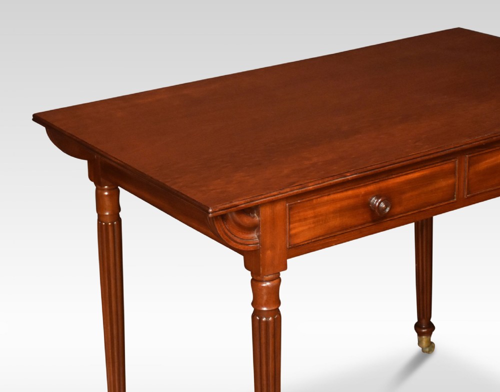 A mahogany writing table featuring two frieze drawers with turned wooden knobs, fluted turned legs, side scroll details, and brass castors. View II