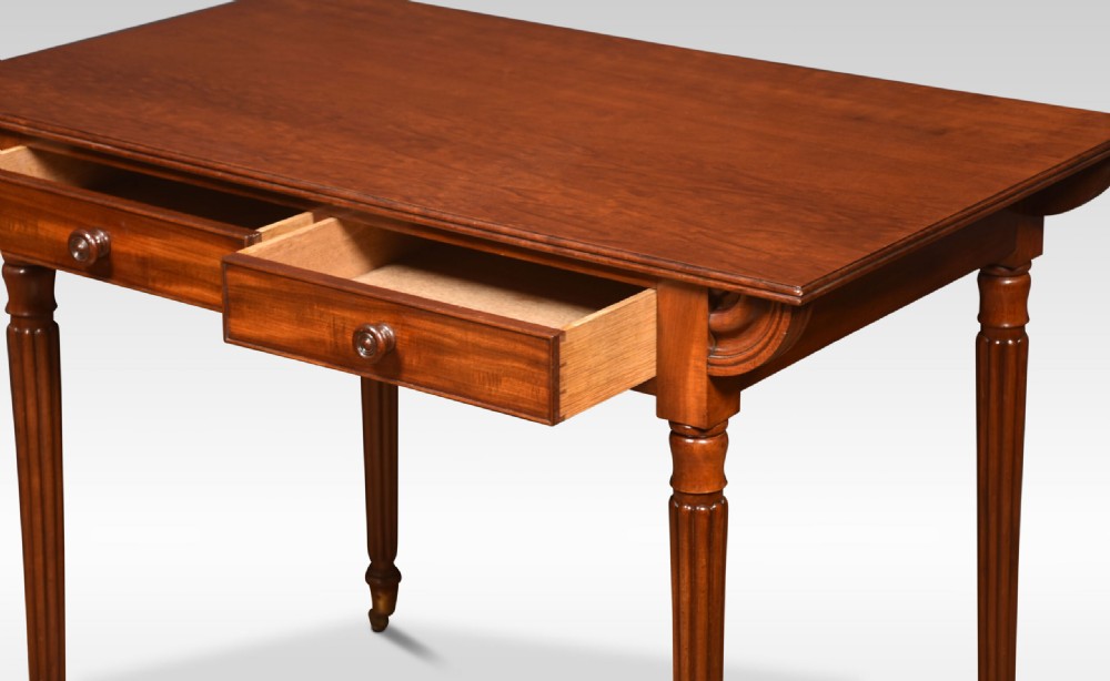 A mahogany writing table featuring two frieze drawers with turned wooden knobs, fluted turned legs, side scroll details, and brass castors. View V