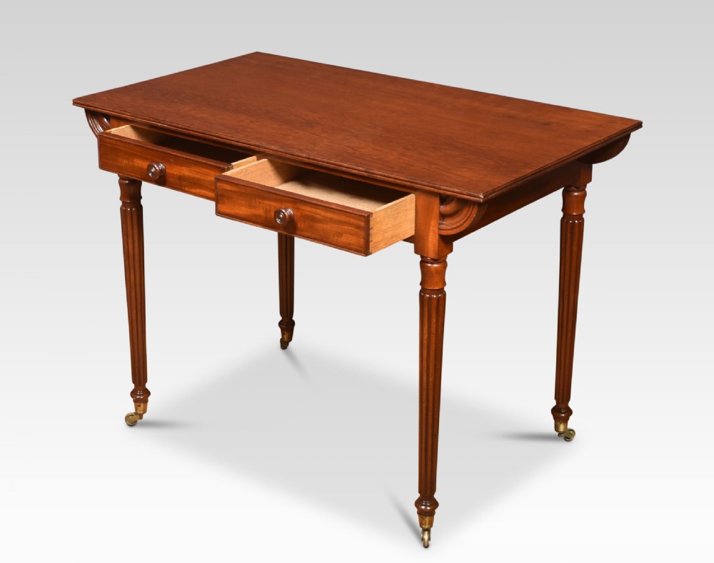 A mahogany writing table featuring two frieze drawers with turned wooden knobs, fluted turned legs, side scroll details, and brass castors. View VI