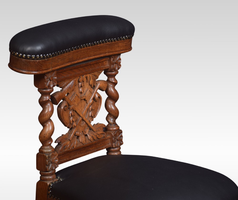 A carved oak side chair with barley twist supports, dark leather padded top rail and seat, and a central coat of arms motif on the backrest. View III