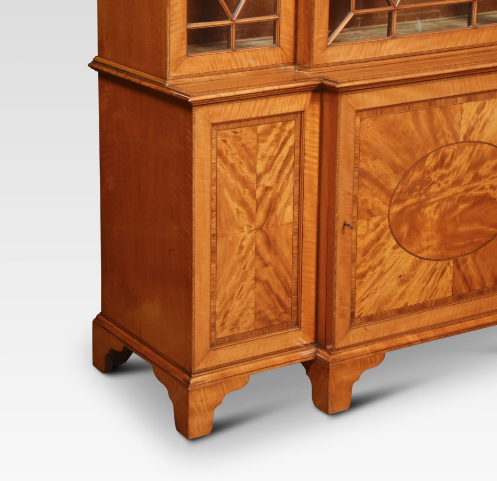 A tall Sheraton Revival satinwood breakfront bookcase featuring geometric astragal glazed upper doors above panelled lower cupboards. View IX