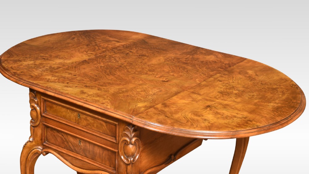 An antique Victorian figured walnut work table featuring two drawers, carved side scrolls, cabriole legs, and brass castors. View IV