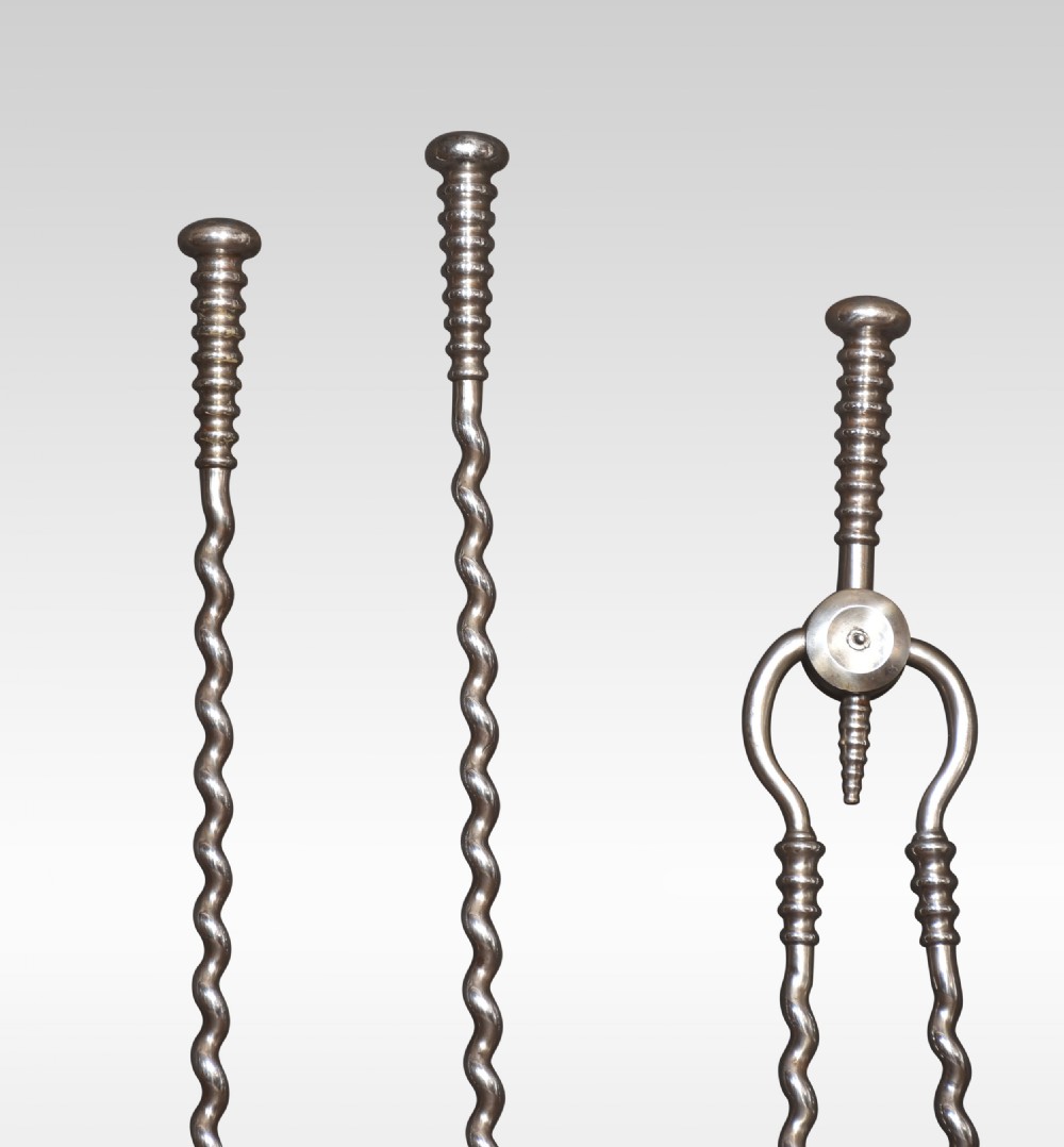 A three-piece set of polished steel fireplace tools comprising a poker, shovel, and tongs with barley twist shafts and turned handles. View II