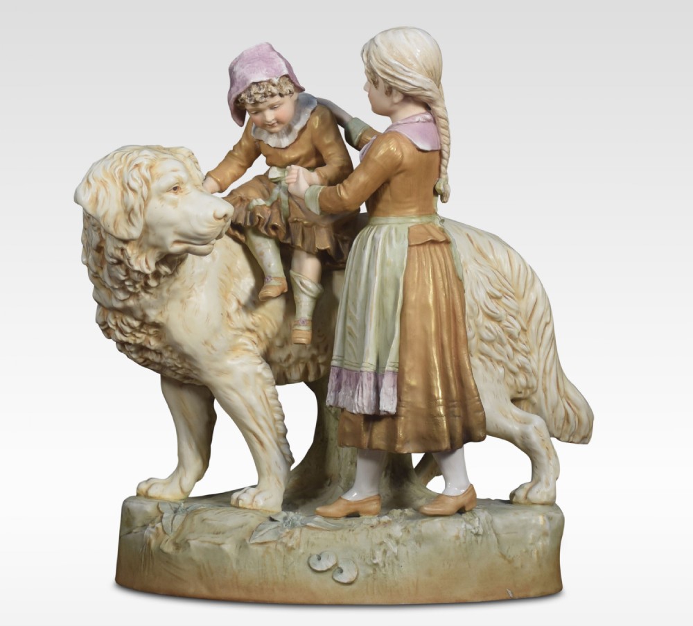 A Royal Dux porcelain figural group depicting two children interactively seated upon and standing beside a large long-haired dog.