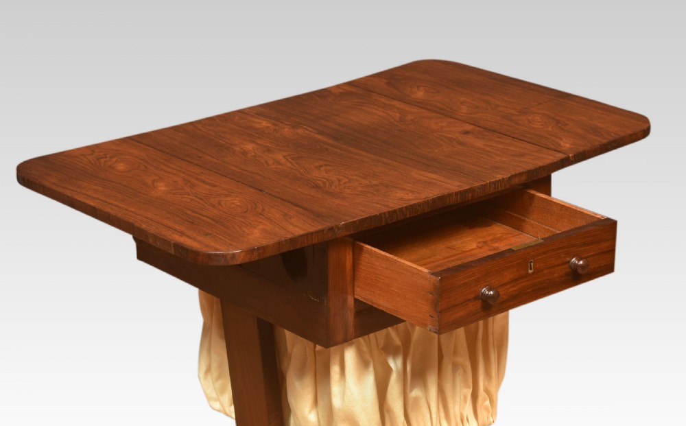 An antique rosewood sewing table featuring a drop-leaf top, a single drawer above a pleated cream fabric basket, and a turned central column on carved paw feet. View VIII