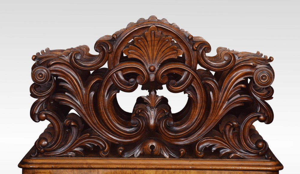 A carved Victorian figured walnut Canterbury featuring three carved scrollwork dividers, a single base drawer with wooden knobs, and cabriole legs on brass castors. View III