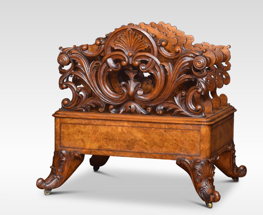 A carved Victorian figured walnut Canterbury featuring three carved scrollwork dividers, a single base drawer with wooden knobs, and cabriole legs on brass castors. View V