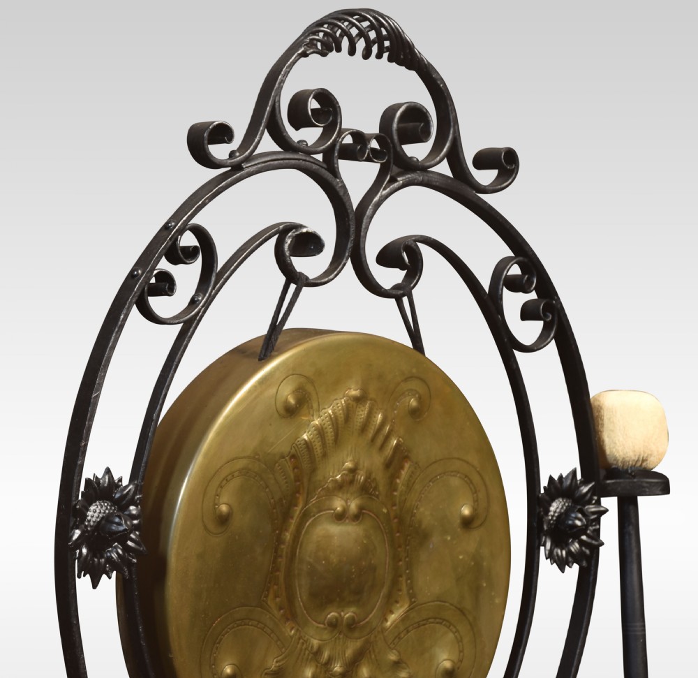 An Art Nouveau freestanding brass dinner gong suspended inside an ornamental dark metal scrollwork frame with an attached mallet striker. View II