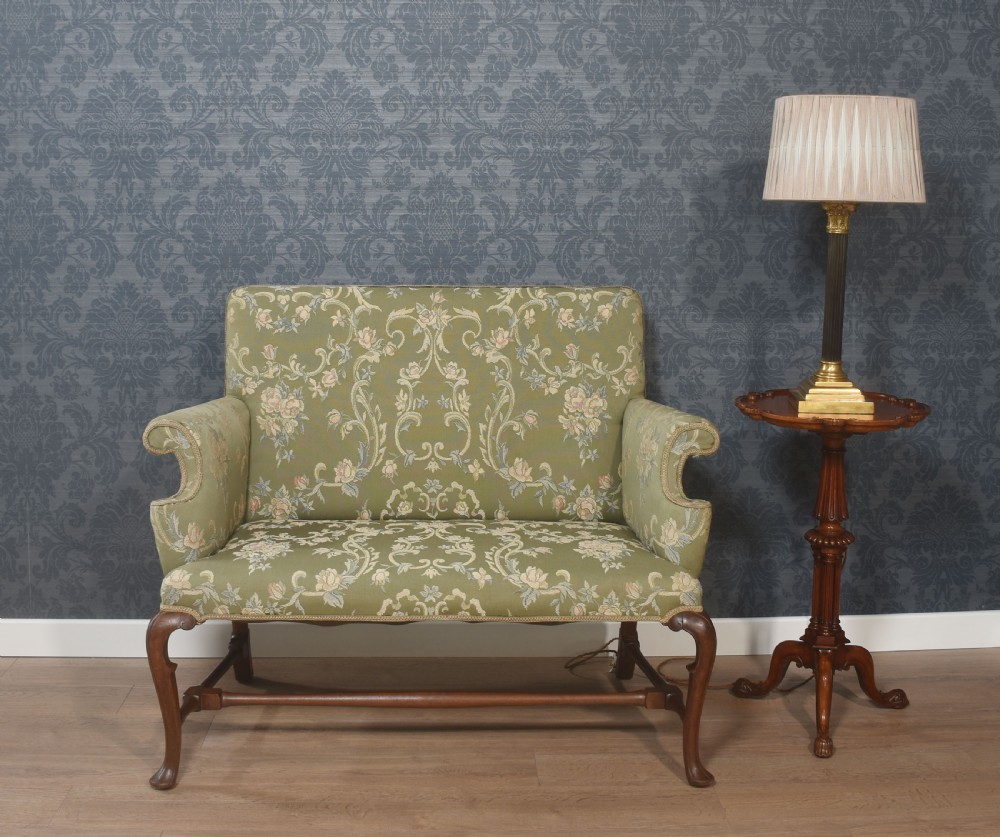 A two-seat Queen Anne style settee upholstered in green floral damask fabric with polished walnut cabriole legs and stretchers.