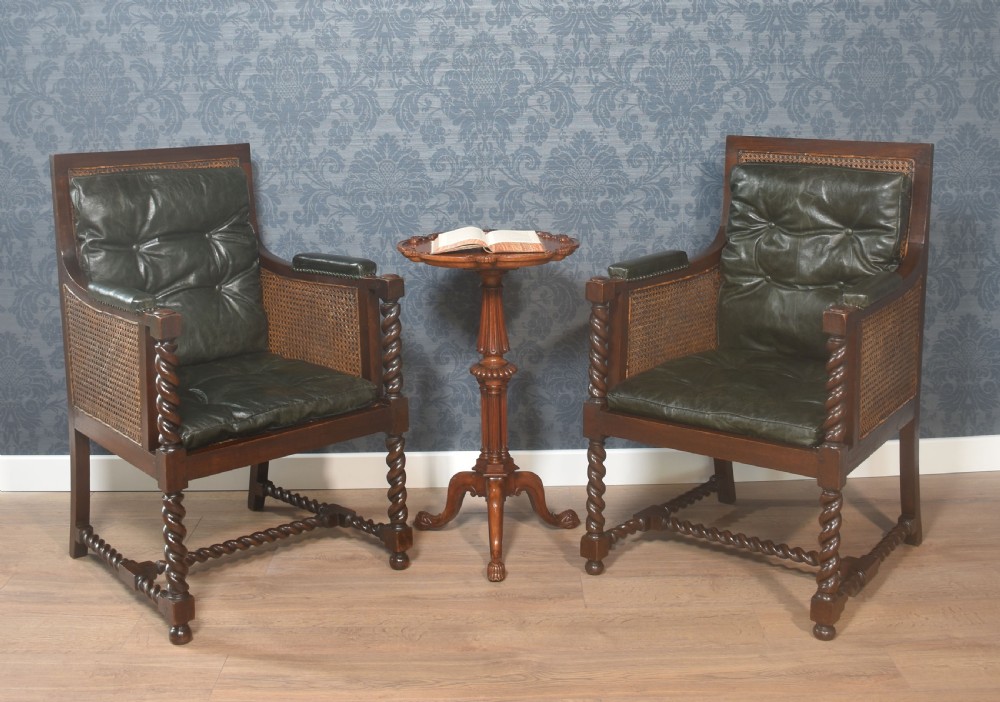 A pair of dark oak bergere library armchairs featuring barley twist legs, woven cane side panels, and deep-tufted dark green leather cushions.