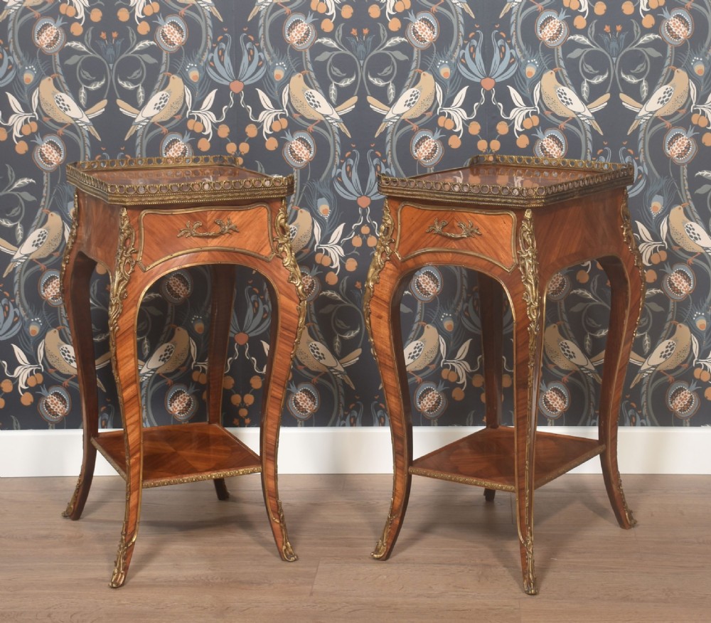 A pair of French Louis XV style walnut bedside tables featuring slender cabriole legs, brass mounts, single drawer handles, lower shelves, and pierced brass galleries around the tops.