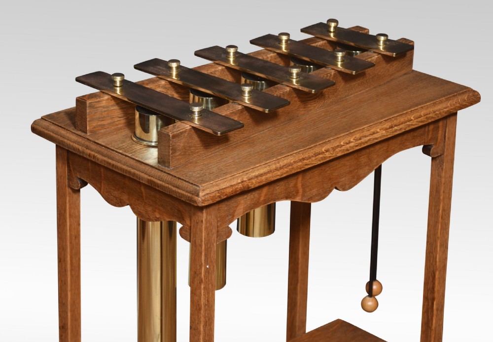 An antique oak glockenspiel stand featuring brass tone bars mounted on top, suspended tubular brass resonators underneath, and two mallets hanging at the side. View III