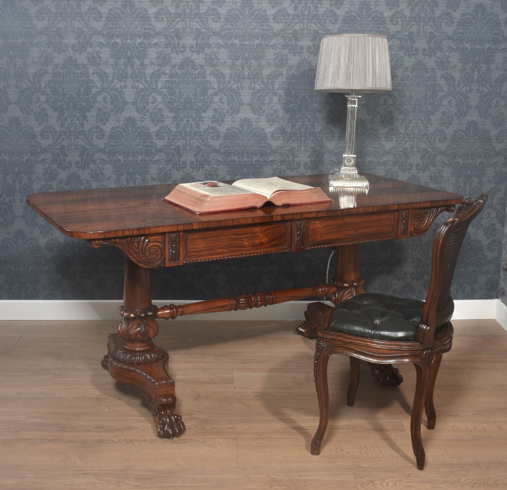 A Regency rosewood library table featuring a rectangular top, twin carved pedestal supports, a turned cross stretcher, and lion paw feet.