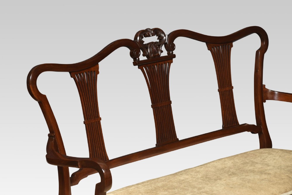 An antique carved mahogany settee featuring a triple fluted splat backrest, sweeping armrests, and a light beige upholstered seat. View III