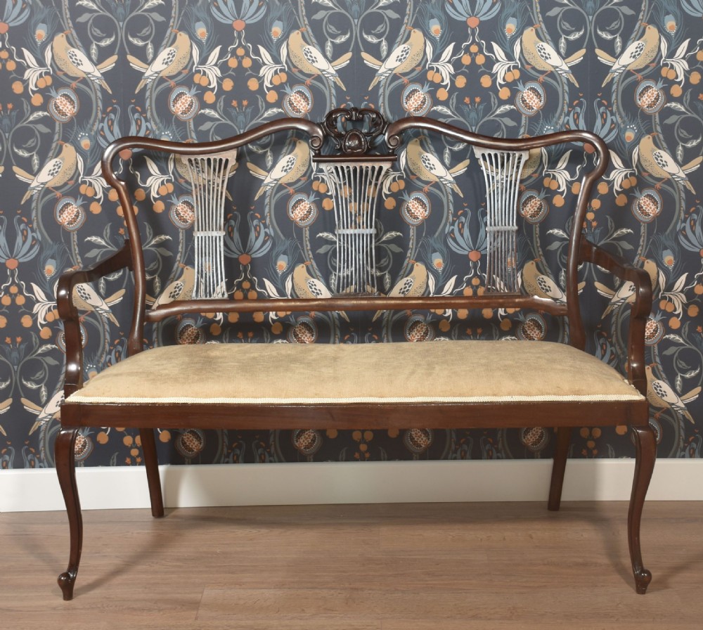 An antique carved mahogany settee featuring a triple fluted splat backrest, sweeping armrests, and a light beige upholstered seat. View VI