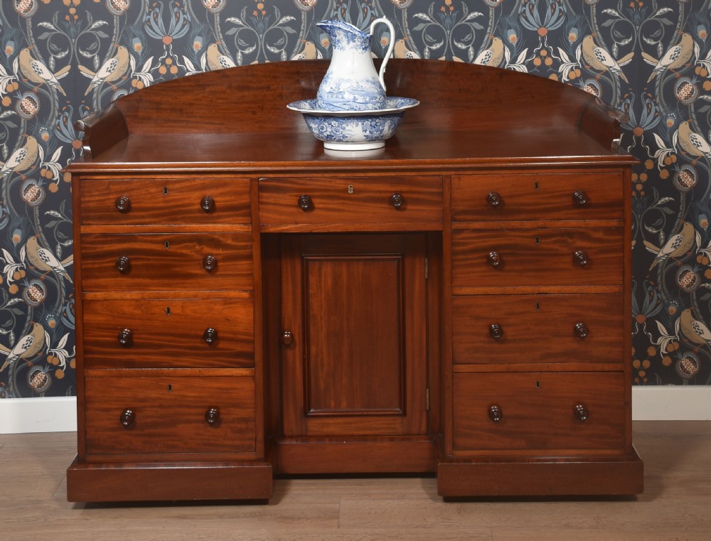 A nineteenth-century mahogany kneehole dressing table featuring an arched gallery upstand, nine drawers with turned handles, and a central cupboard door.