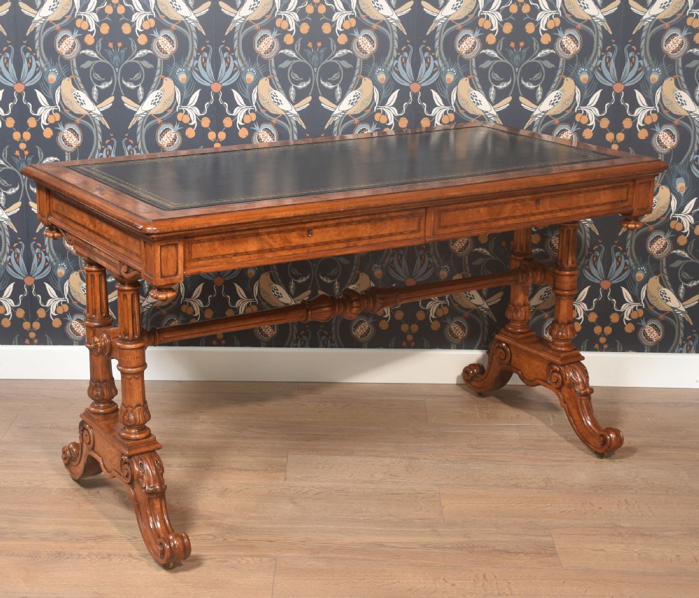 A Victorian walnut writing desk with an inset dark leather surface, frieze drawers, turned side columns, and carved scroll trestle feet.
