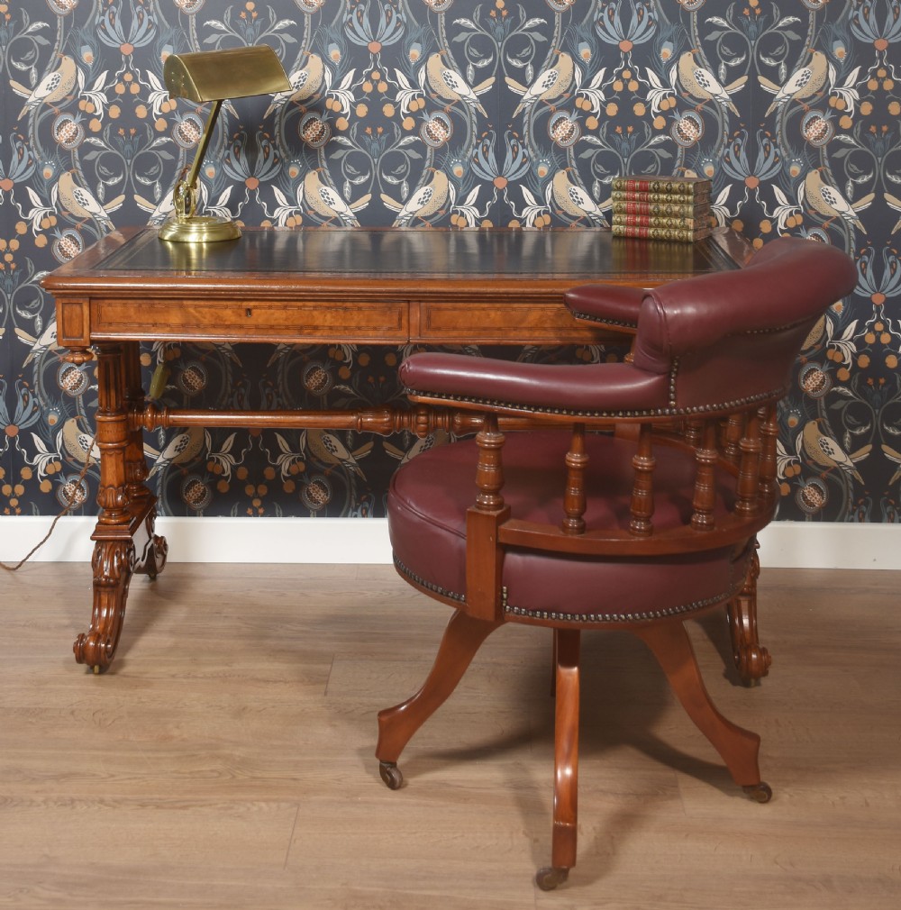 A Victorian walnut writing desk with an inset dark leather surface, frieze drawers, turned side columns, and carved scroll trestle feet. View V