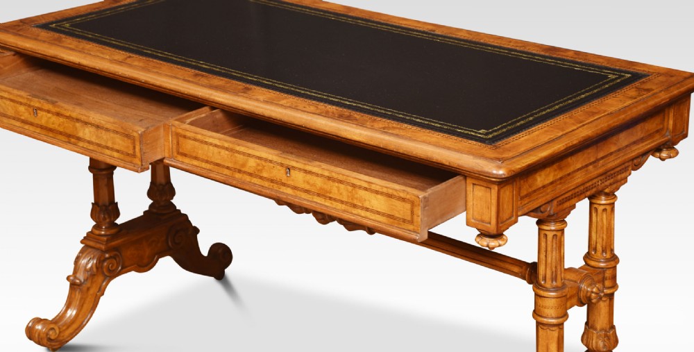 A Victorian walnut writing desk with an inset dark leather surface, frieze drawers, turned side columns, and carved scroll trestle feet. View VII