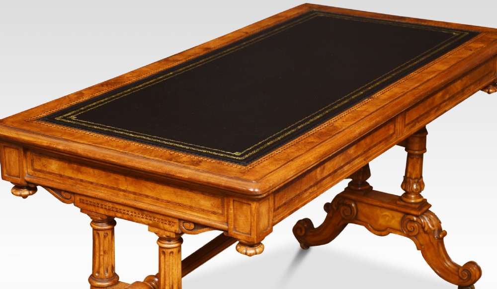 A Victorian walnut writing desk with an inset dark leather surface, frieze drawers, turned side columns, and carved scroll trestle feet. View X