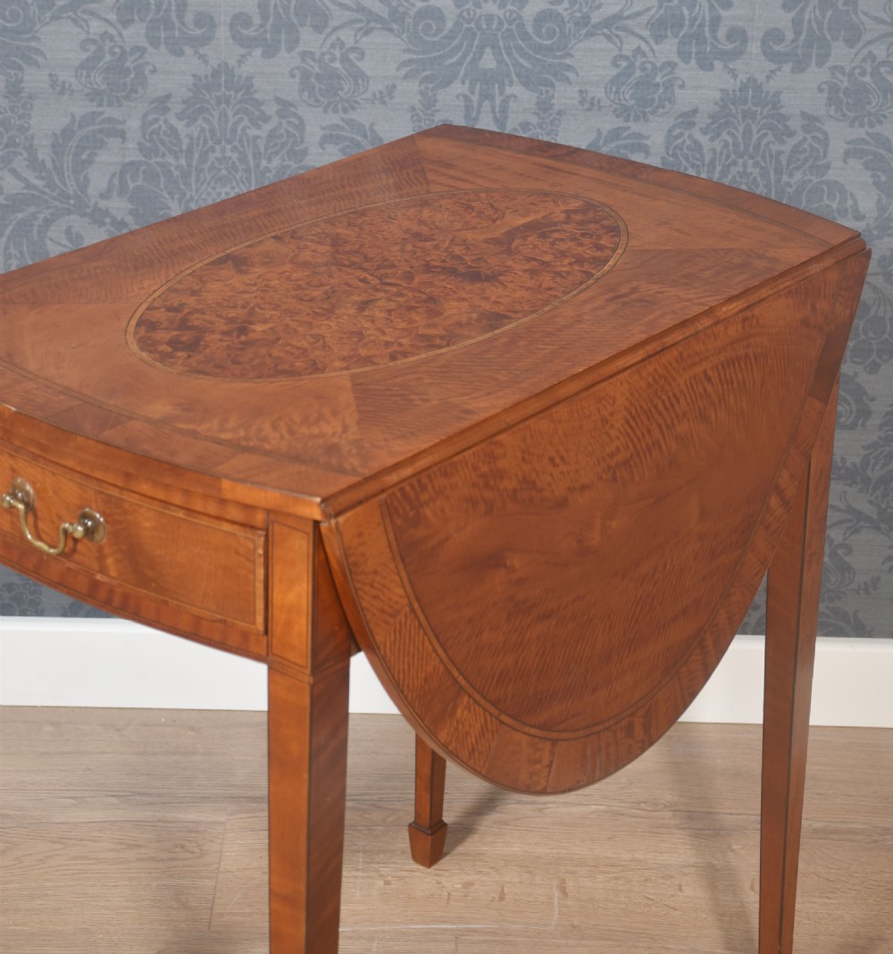 A George III style satinwood Pembroke table featuring an oval burr veneer central inlay, drop-leaf sides, a single drawer with a brass handle, and square tapered legs terminating in spade feet. View III
