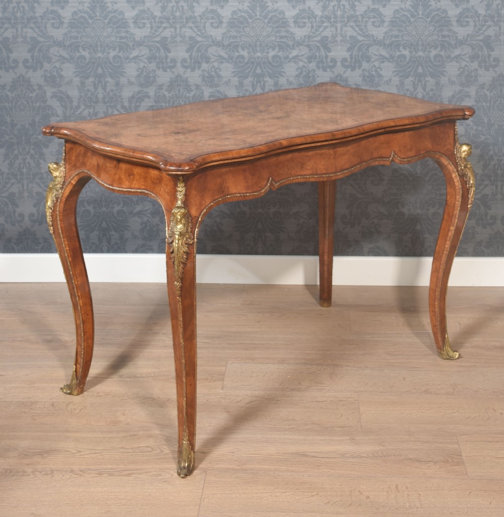 A nineteenth-century burr walnut card table featuring a serpentine top, carved frieze, cabriole legs, and ornate gilt bronze ormolu mounts.