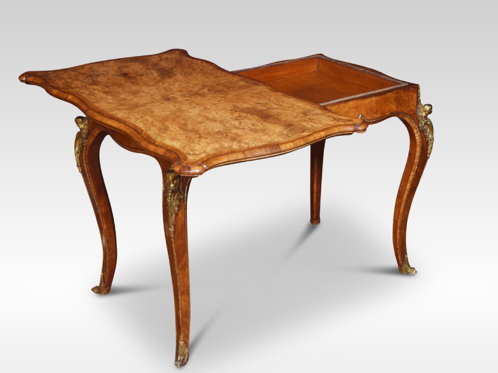 A nineteenth-century burr walnut card table featuring a serpentine top, carved frieze, cabriole legs, and ornate gilt bronze ormolu mounts. View V